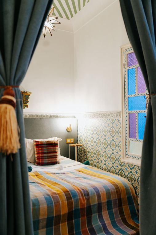 Bedroom with a colourful blanket, tiles and stained glass