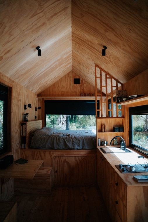 Plywood cabin interior with bed by the window and kitchen